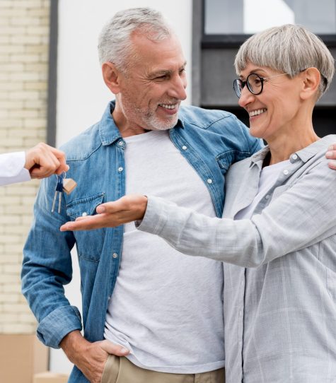 cropped view of broker giving keys of new house to smiling man and woman